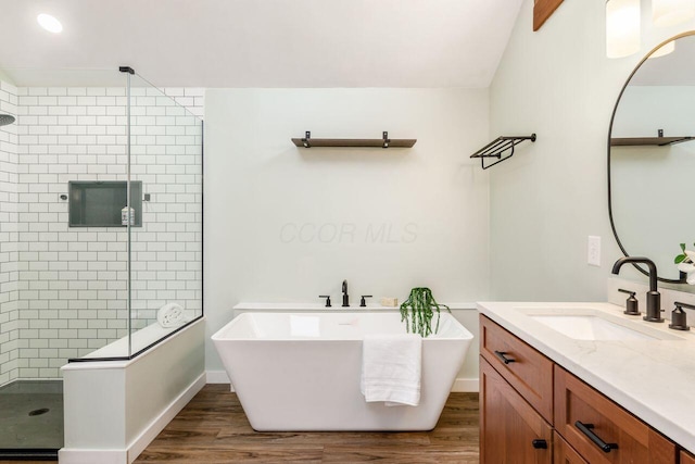 bathroom featuring vanity, wood finished floors, baseboards, a freestanding tub, and a shower stall