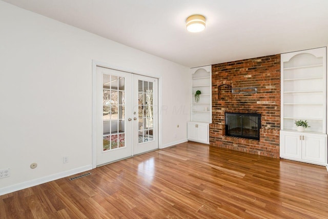 unfurnished living room with built in features, visible vents, a brick fireplace, and french doors