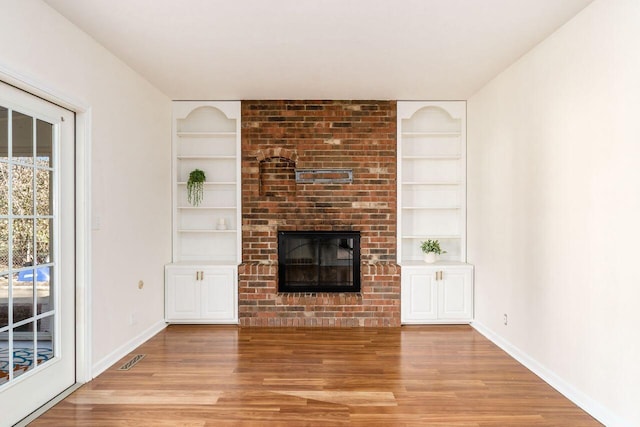 unfurnished living room with light wood-style flooring, a fireplace, baseboards, and built in shelves