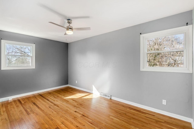 empty room featuring ceiling fan, visible vents, baseboards, and wood finished floors