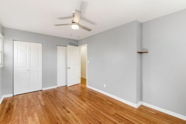 unfurnished bedroom with baseboards, multiple closets, ceiling fan, and light wood finished floors