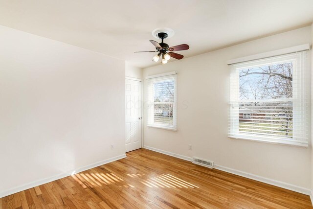 unfurnished room with a ceiling fan, light wood-style floors, visible vents, and baseboards