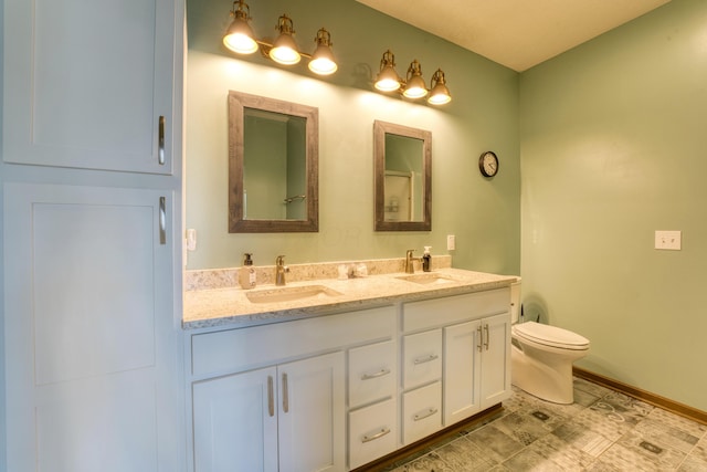 bathroom featuring double vanity, toilet, baseboards, and a sink