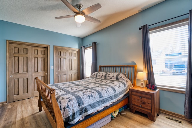 bedroom featuring visible vents, multiple closets, a ceiling fan, a textured ceiling, and light wood finished floors