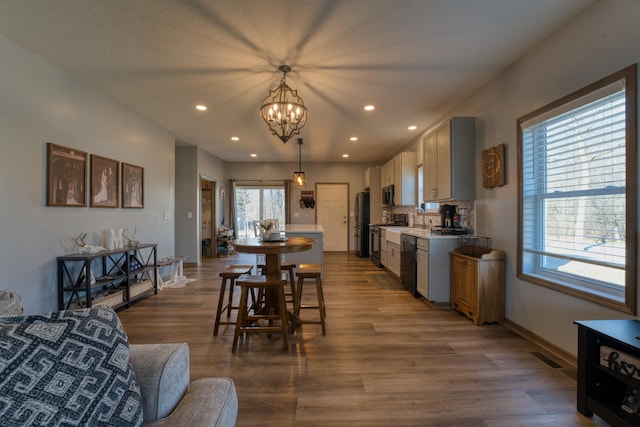 kitchen with baseboards, dark wood-style flooring, decorative backsplash, black appliances, and hanging light fixtures