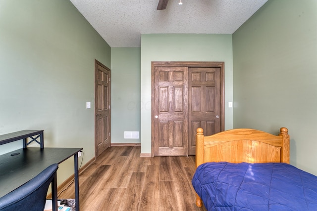 bedroom with visible vents, a textured ceiling, wood finished floors, baseboards, and ceiling fan