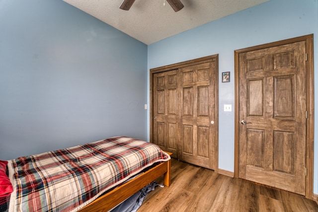 bedroom featuring a textured ceiling, wood finished floors, a closet, lofted ceiling, and ceiling fan