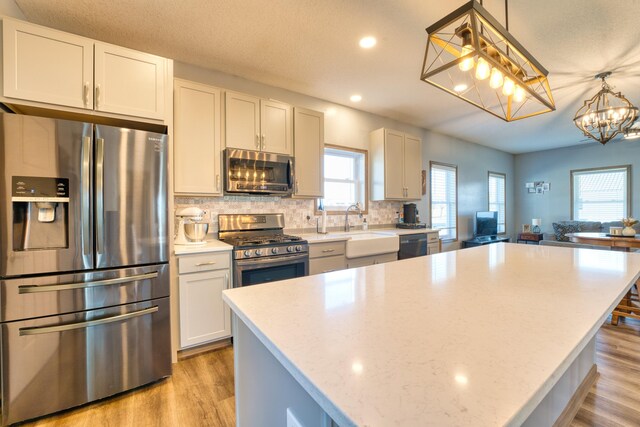 kitchen with light wood finished floors, a kitchen island, appliances with stainless steel finishes, and a sink