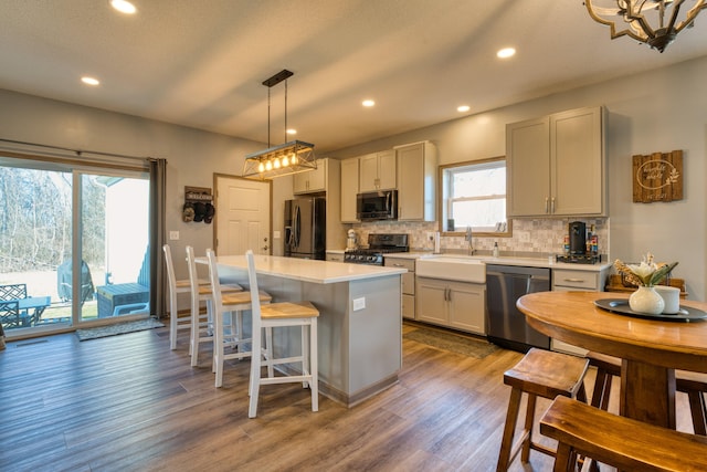 kitchen with wood finished floors, a sink, stainless steel appliances, light countertops, and backsplash