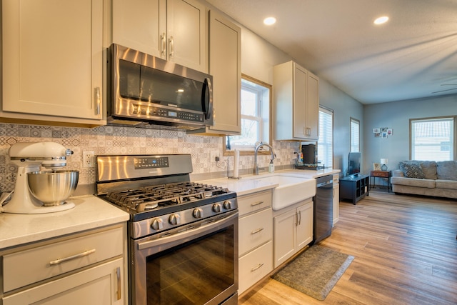 kitchen featuring backsplash, open floor plan, plenty of natural light, stainless steel appliances, and a sink