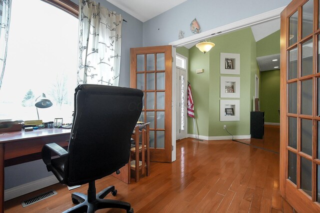 office area featuring lofted ceiling, a fireplace, wood finished floors, visible vents, and baseboards