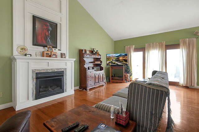 living area with baseboards, vaulted ceiling, a premium fireplace, and wood finished floors