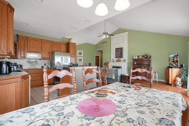 dining area with light tile patterned floors, ceiling fan, a fireplace, and vaulted ceiling