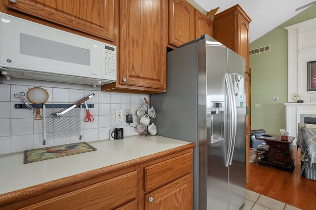 kitchen featuring stainless steel fridge, visible vents, decorative backsplash, white microwave, and light countertops