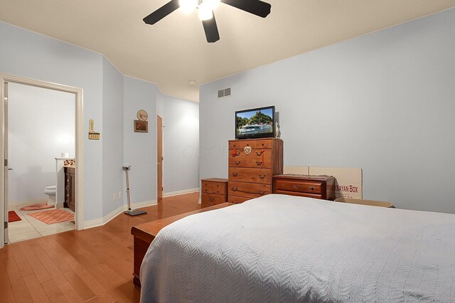 bedroom featuring visible vents, a ceiling fan, ensuite bath, wood finished floors, and baseboards