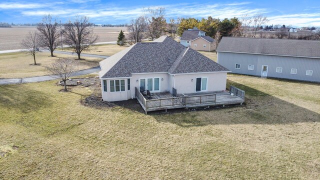 rear view of house with stucco siding, a deck, a lawn, and roof with shingles