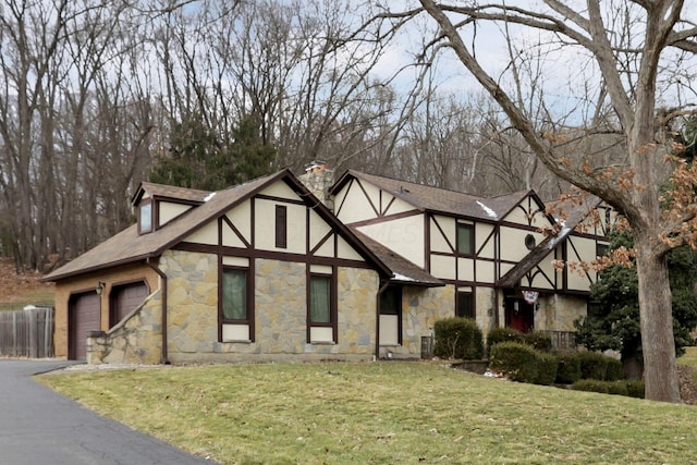 english style home with aphalt driveway, a garage, stucco siding, a front lawn, and a chimney