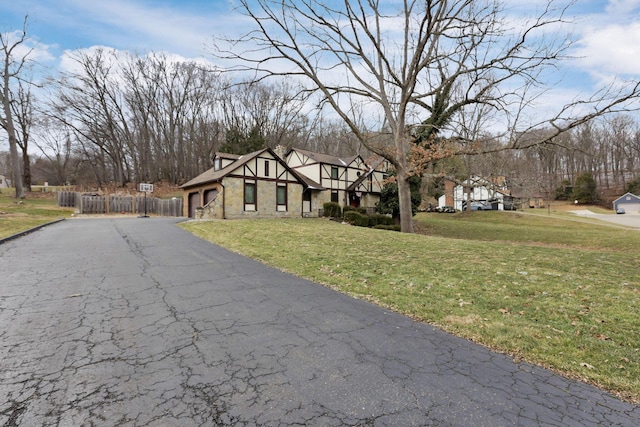 english style home with driveway, a garage, stone siding, fence, and a front yard