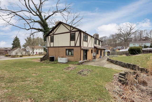 view of side of property with a lawn, stucco siding, a chimney, fence, and brick siding