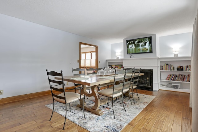 dining area with a fireplace, wood-type flooring, and baseboards