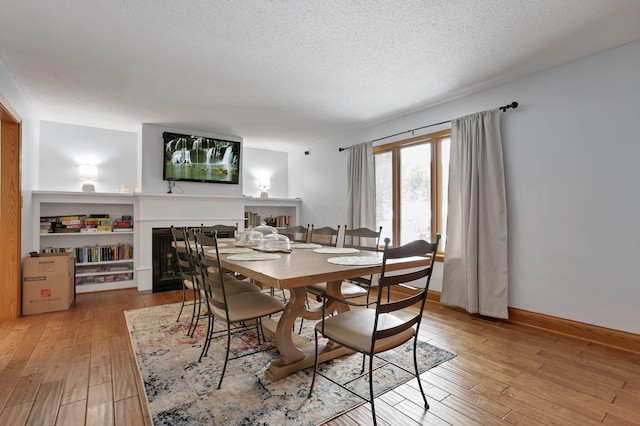 dining room with a textured ceiling, light wood-type flooring, a multi sided fireplace, and baseboards