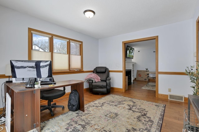 office space featuring a fireplace, wood-type flooring, visible vents, and baseboards