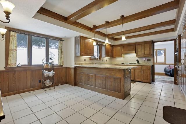 kitchen with beam ceiling, decorative light fixtures, light tile patterned floors, brown cabinetry, and a peninsula