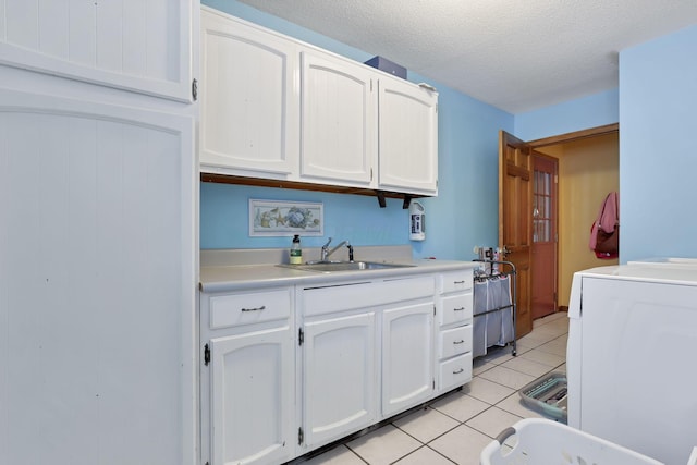 kitchen with light tile patterned floors, washer / clothes dryer, white cabinetry, a sink, and a textured ceiling