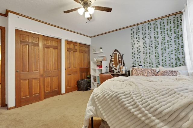 bedroom with ceiling fan, ornamental molding, carpet flooring, and multiple closets