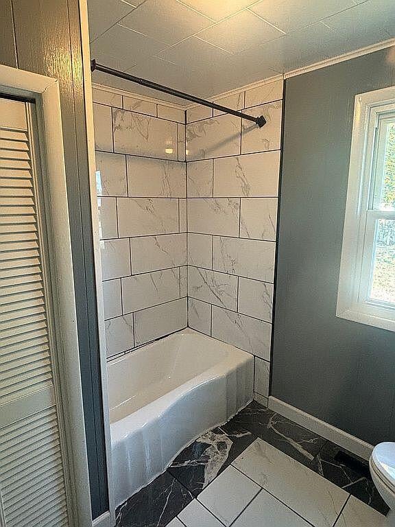 bathroom featuring marble finish floor, bathtub / shower combination, toilet, and baseboards