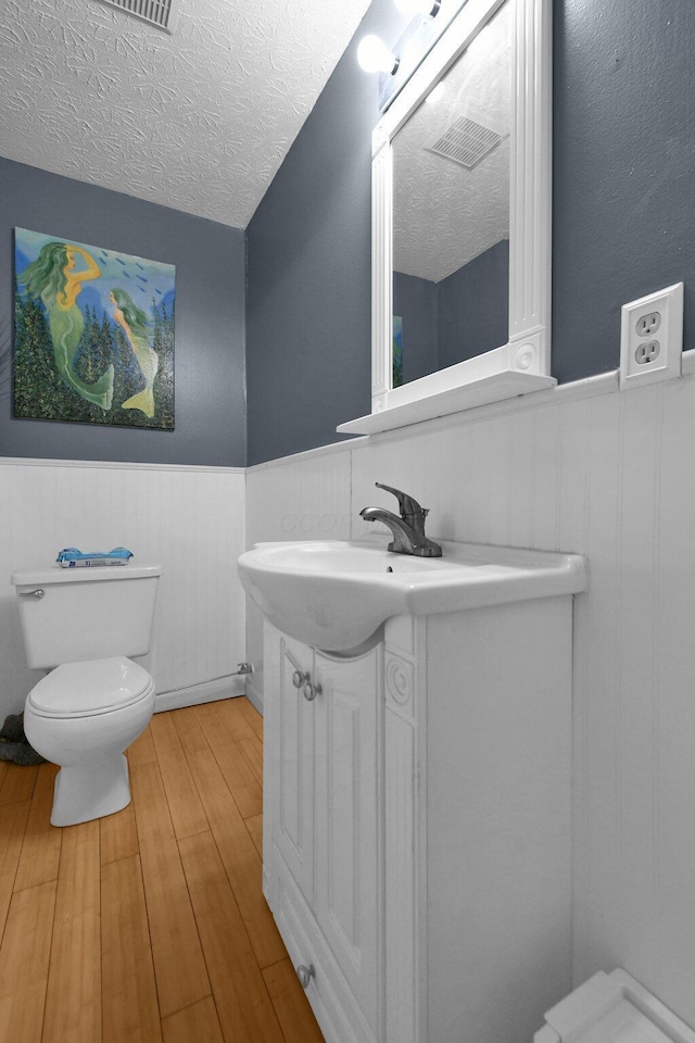 bathroom featuring wainscoting, a textured ceiling, toilet, and wood finished floors