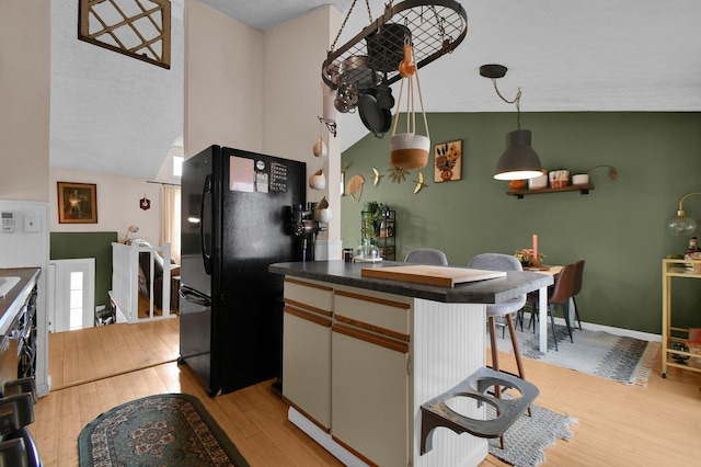 kitchen with light wood finished floors, baseboards, dark countertops, freestanding refrigerator, and vaulted ceiling