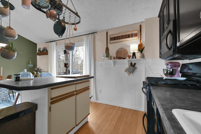 kitchen featuring a textured ceiling, vaulted ceiling, black range with gas stovetop, light wood finished floors, and dark countertops