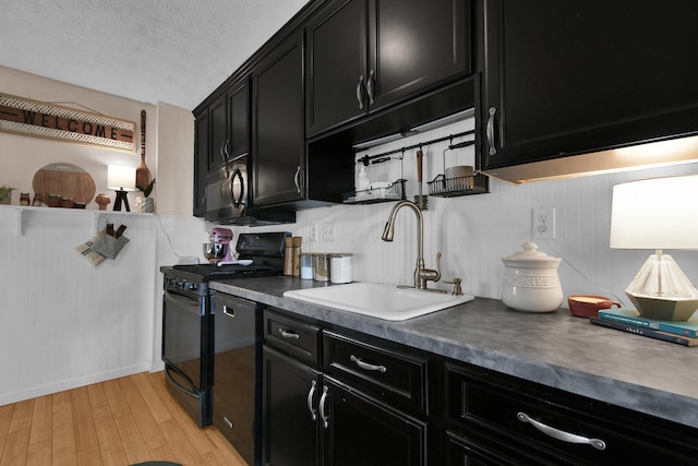 kitchen featuring light wood-type flooring, dark cabinetry, a sink, and black appliances