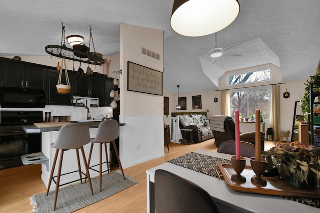 dining space featuring visible vents, a ceiling fan, lofted ceiling, a textured ceiling, and light wood-style floors