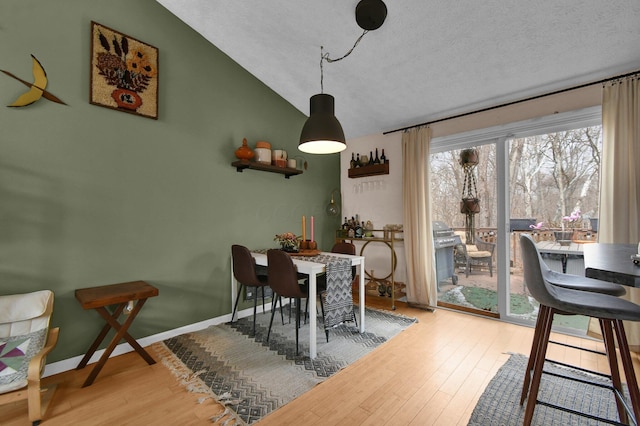 dining area with vaulted ceiling, a textured ceiling, wood finished floors, and baseboards