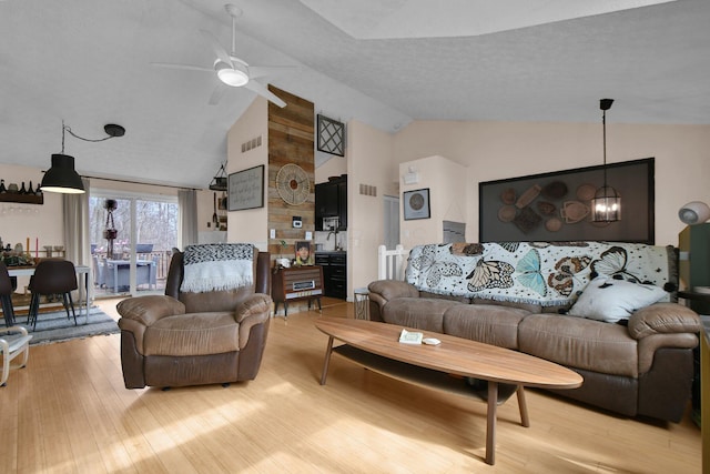 living area featuring light wood-type flooring, visible vents, vaulted ceiling, and ceiling fan with notable chandelier