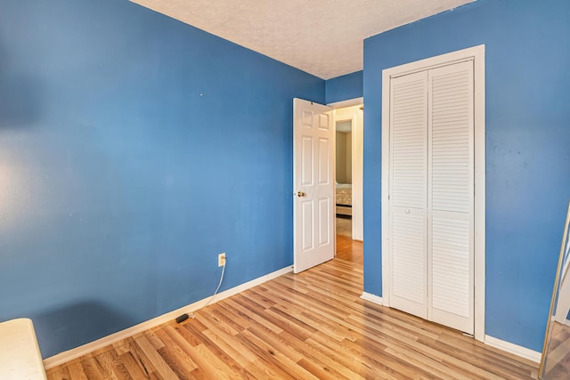 unfurnished bedroom with baseboards, wood finished floors, a closet, and a textured ceiling