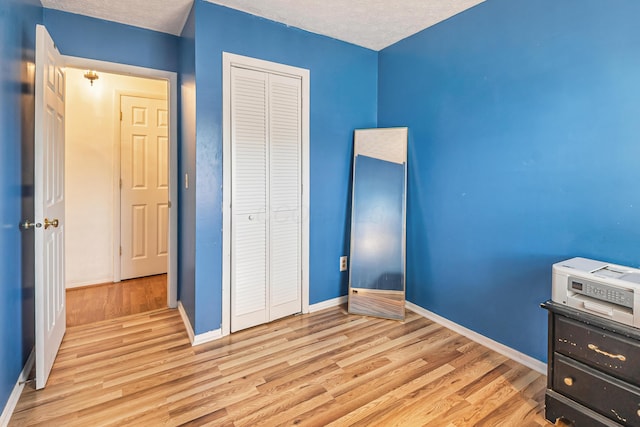 unfurnished bedroom with a closet, a textured ceiling, light wood-type flooring, and baseboards