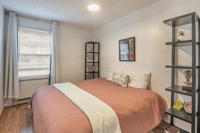 bedroom featuring a textured ceiling, baseboard heating, wood finished floors, and a ceiling fan