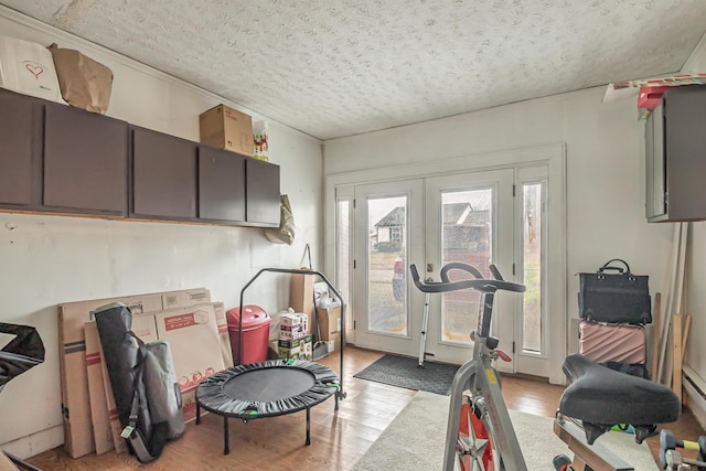 workout area with french doors, light wood-type flooring, and a textured ceiling