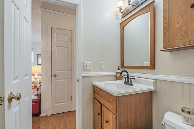 half bath with a wainscoted wall, toilet, wood finished floors, and vanity