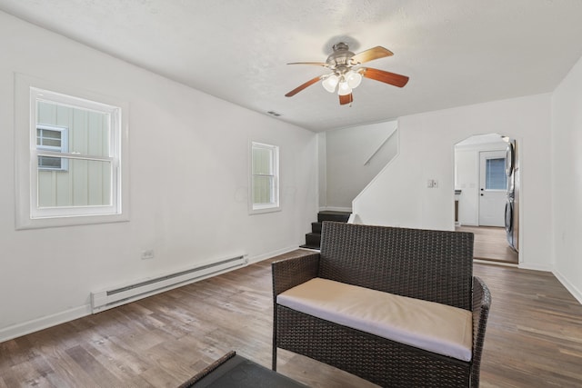 living area with baseboards, arched walkways, stairway, wood finished floors, and a baseboard heating unit