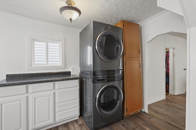 washroom featuring arched walkways, stacked washer and dryer, cabinet space, dark wood-type flooring, and a textured ceiling