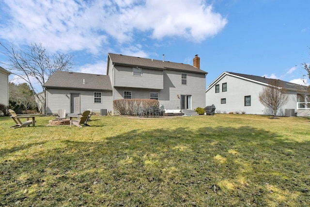 rear view of property featuring entry steps, central air condition unit, a yard, and an outdoor fire pit