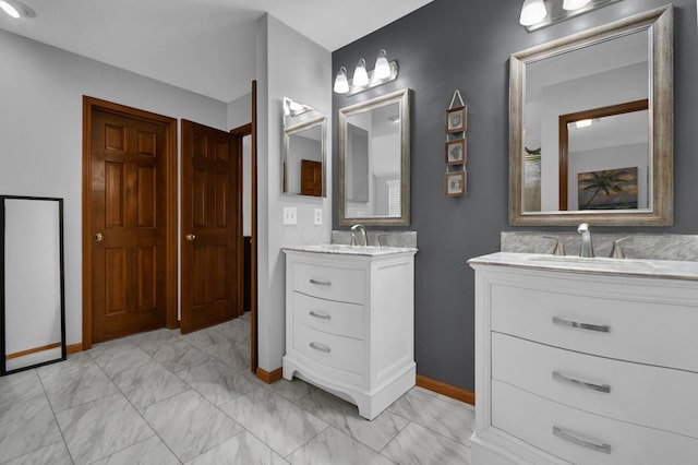 full bathroom with marble finish floor, two vanities, baseboards, and a sink