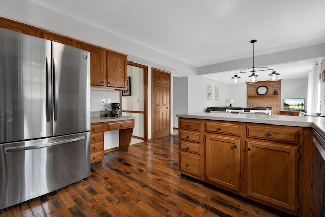 kitchen featuring light countertops, built in desk, freestanding refrigerator, brown cabinetry, and dark wood-style flooring