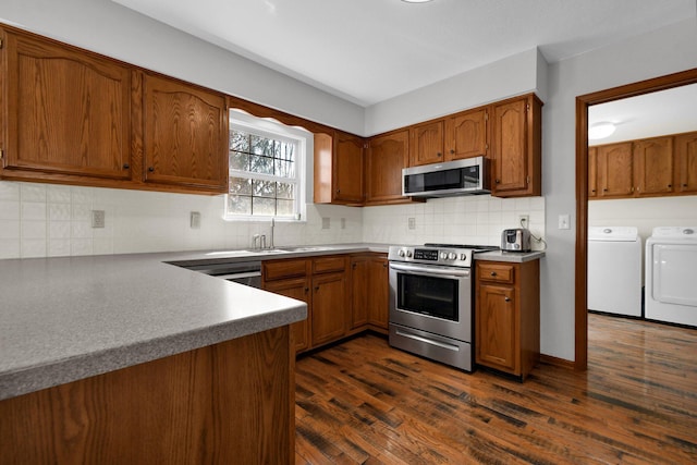 kitchen featuring dark wood-style floors, a sink, stainless steel appliances, washer and dryer, and brown cabinets