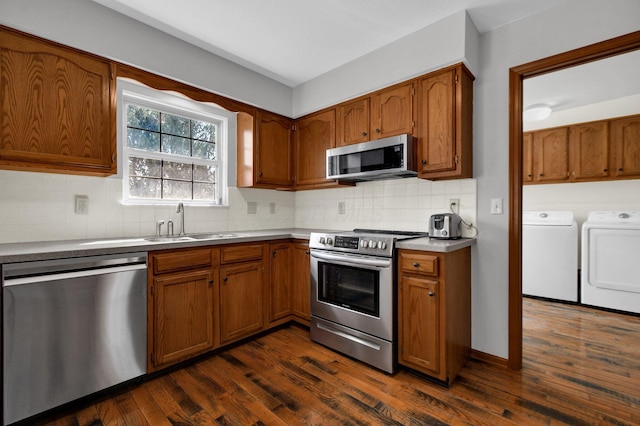 kitchen featuring independent washer and dryer, a sink, dark wood-style floors, stainless steel appliances, and brown cabinetry