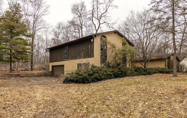 view of side of home featuring a garage, brick siding, and dirt driveway